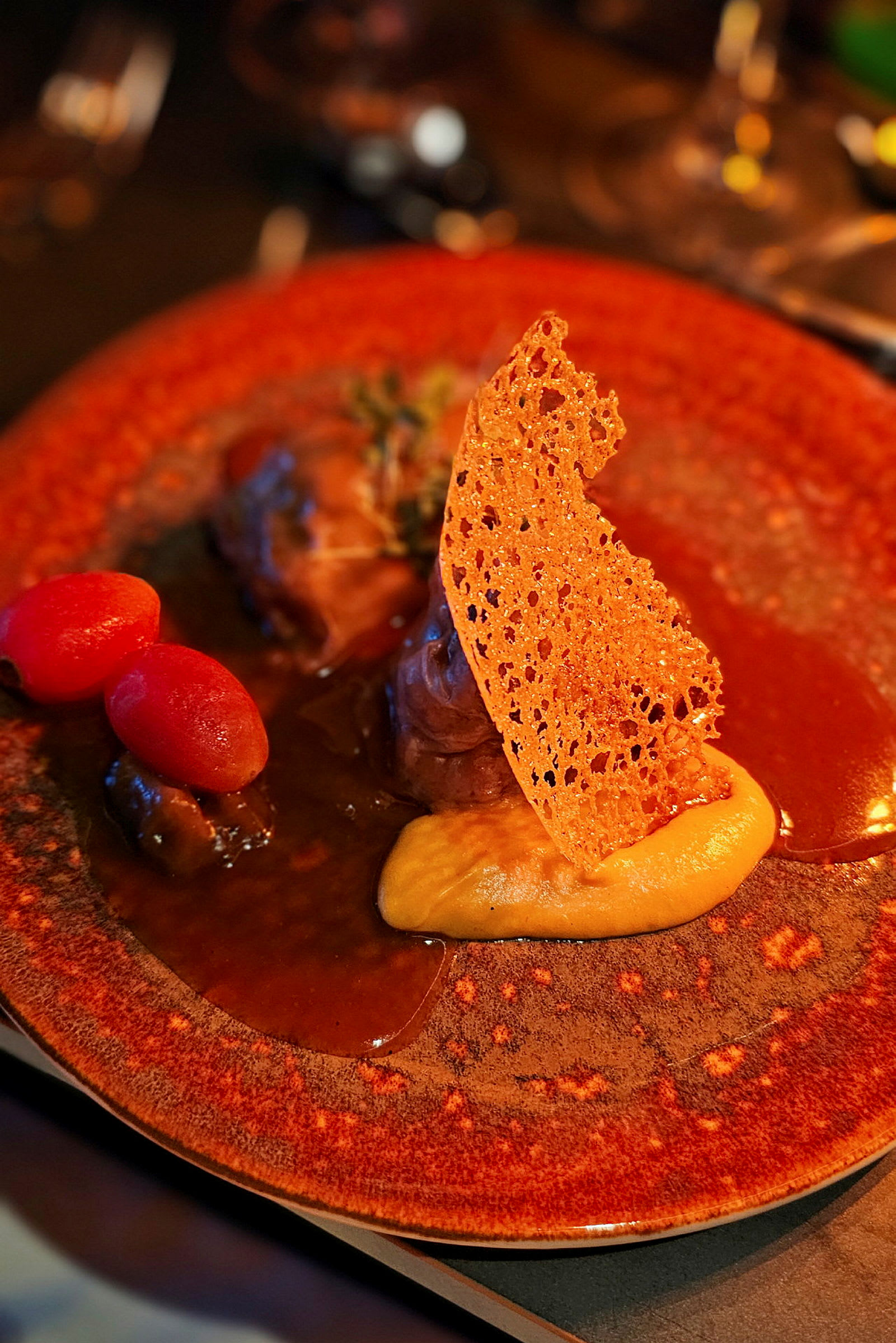En tallrik med en gourmetmåltid upplagt med sås, puré, ett knaprigt dekorationselement och små tomater. (AI-genererad text)