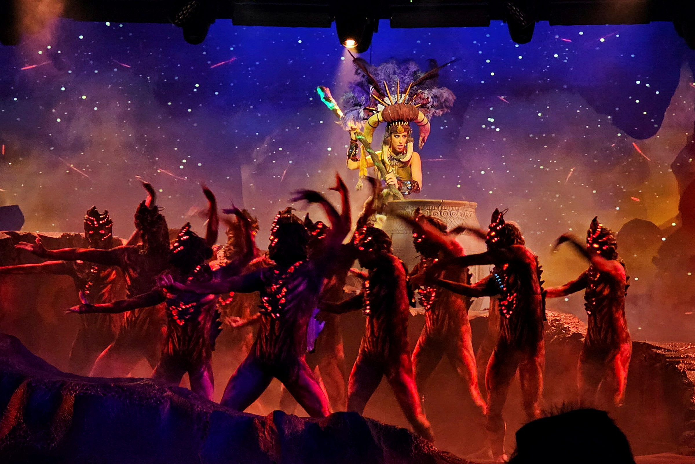 Bild på en scenuppträdande med personer i fantasifull kostym på en färgstark scen. (AI-genererad text)
