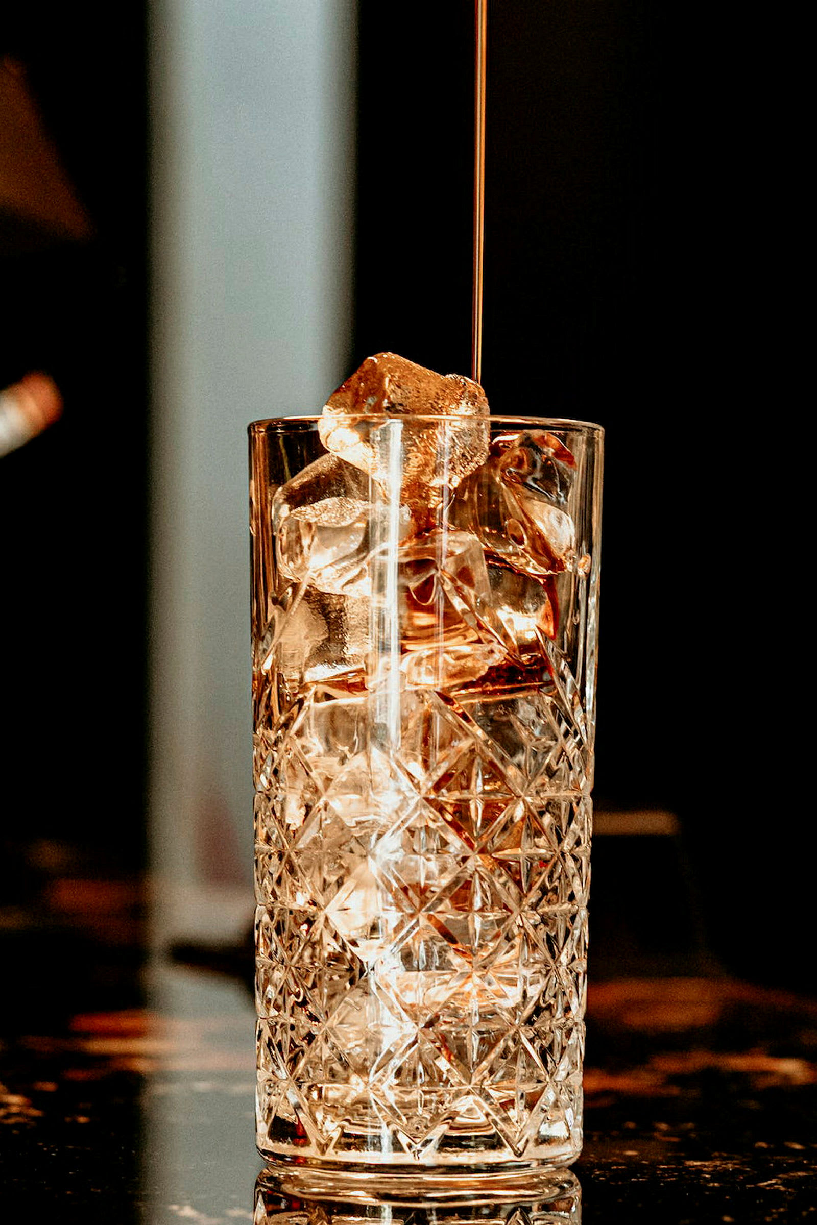 Ett högt glas med isbitar och vätska som hälls i. (AI-genererad text)