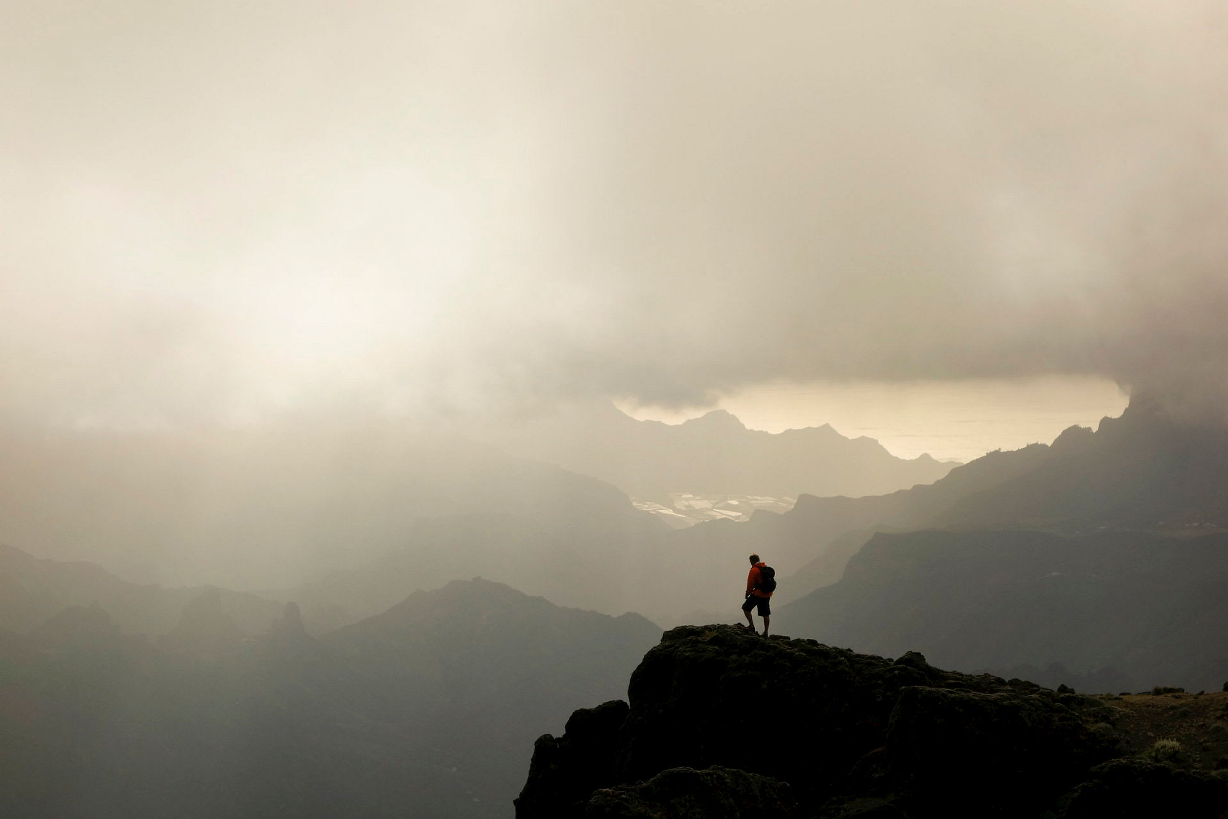 En vandringsman står på en bergstopp med dimmiga dalar och berg i bakgrunden. (AI-genererad text)