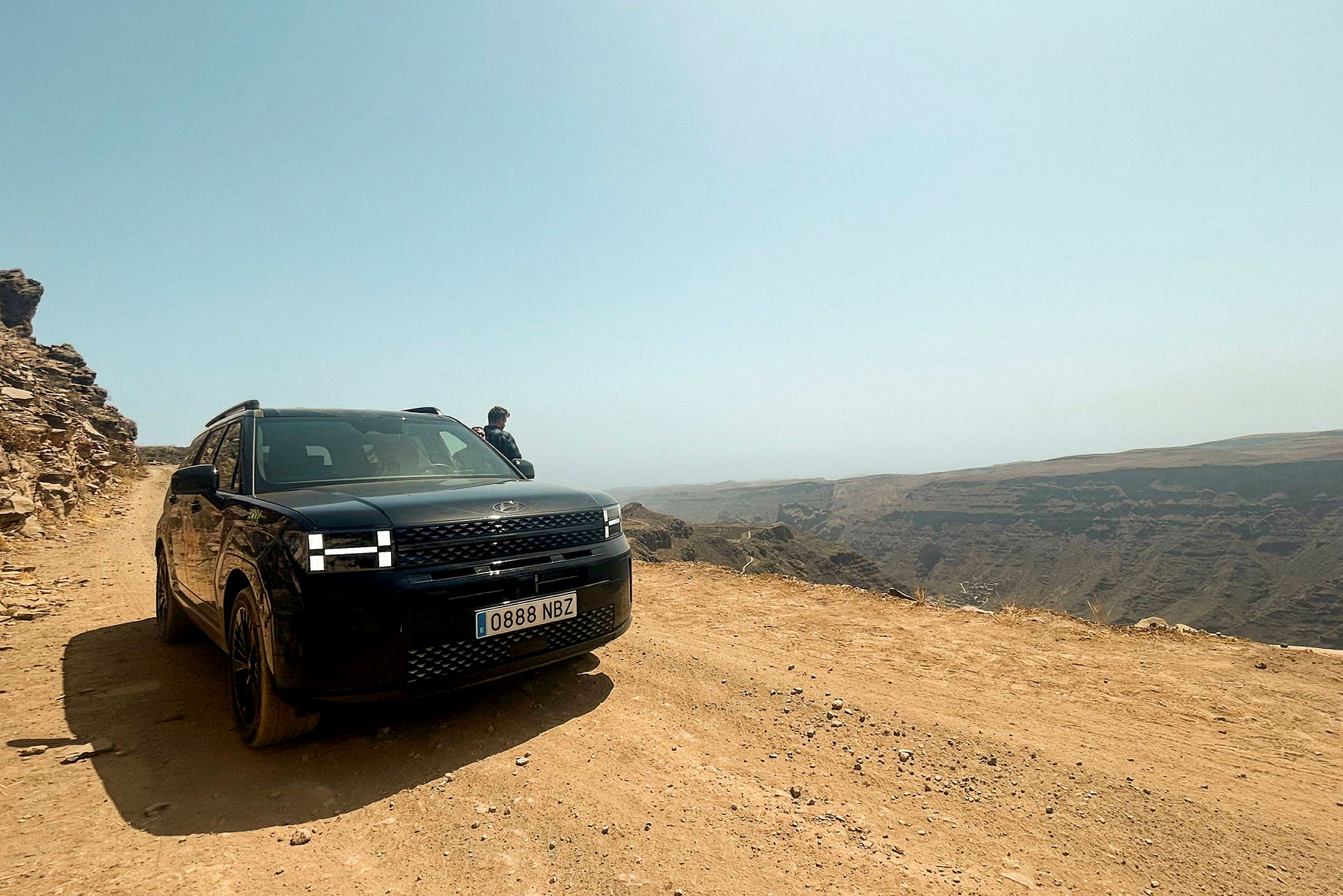 En svart bil står parkerad på en grusväg vid en klippkant. (AI-genererad text)