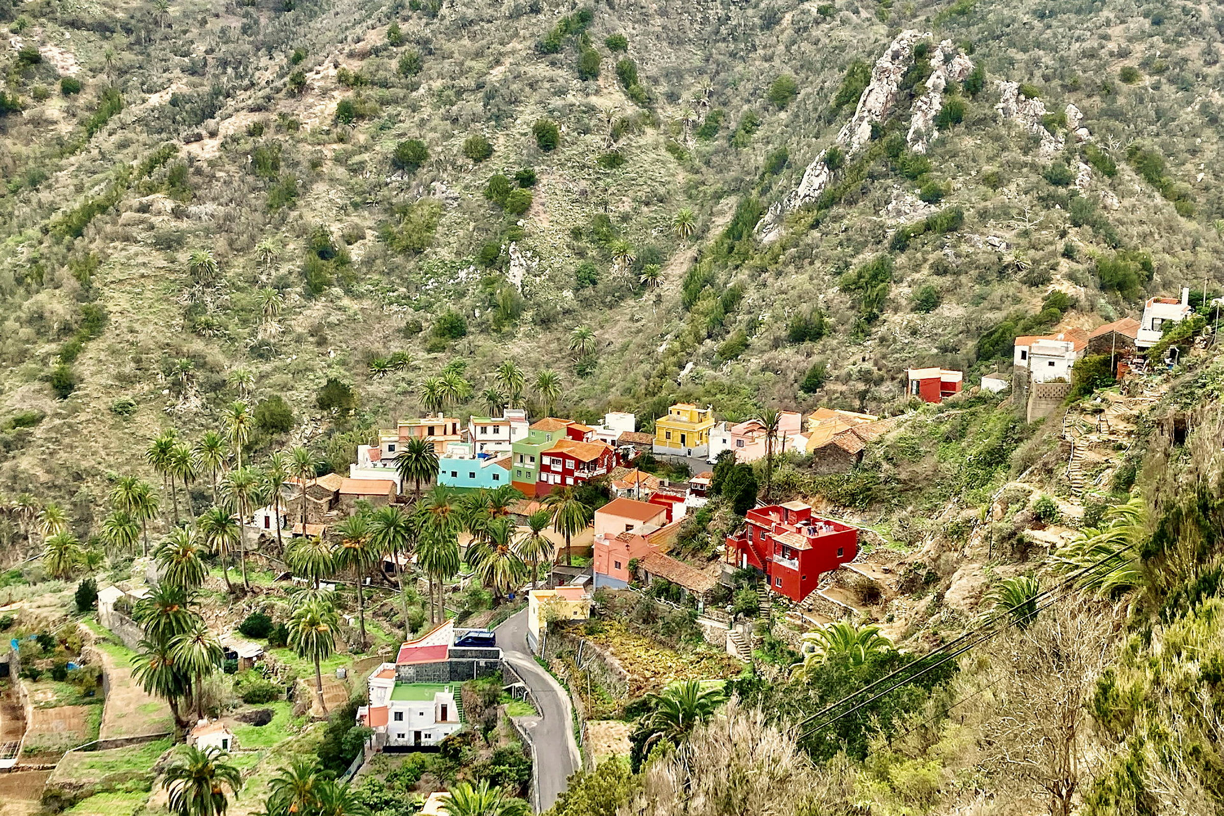 Vy över en by med färgglada hus omgiven av berg och grönska. (AI-genererad text)