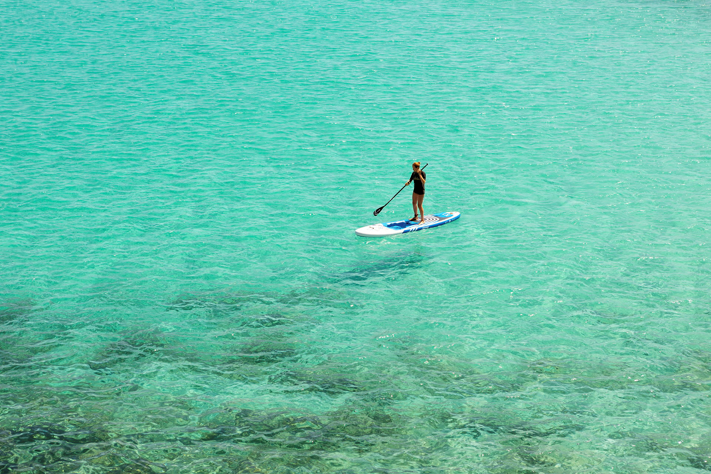 Person som paddlar stående på en paddleboard i klart turkost vatten. (AI-genererad text)