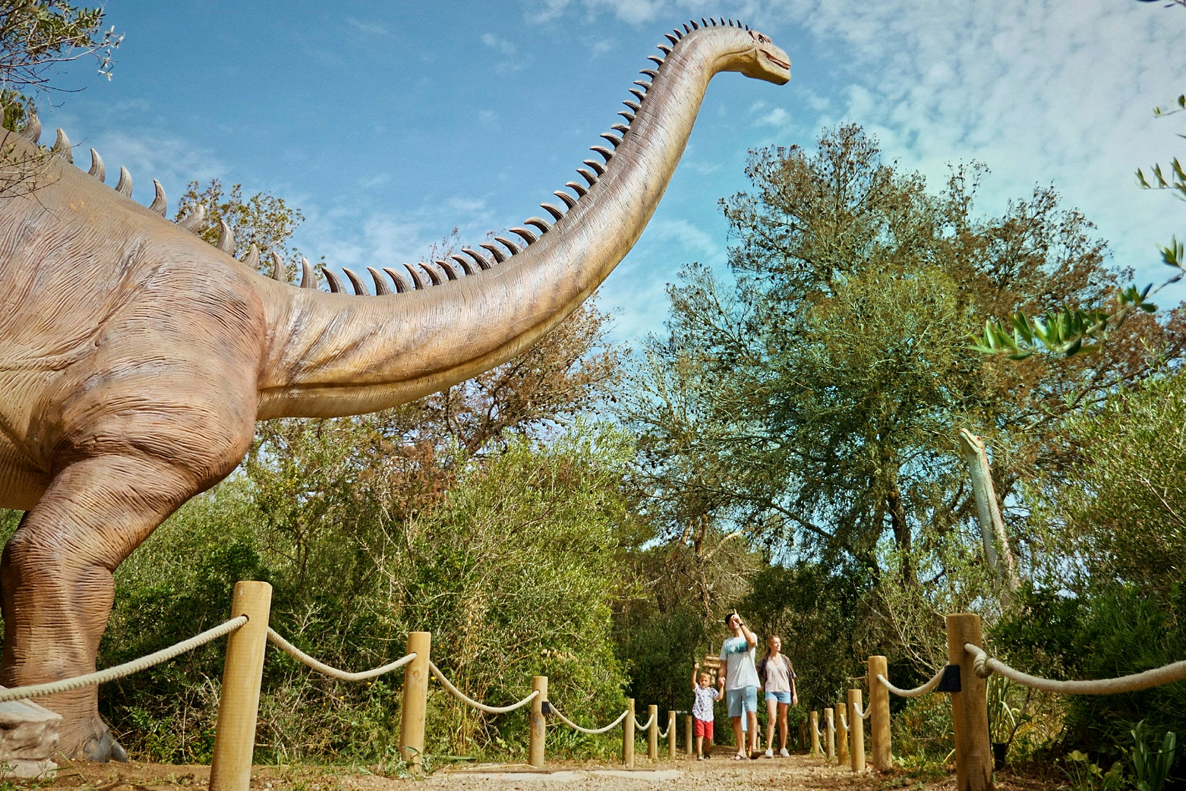 En familj promenerar på en stig intill en stor dinosaurieattrapp i en utomhusutställning. (AI-genererad text)