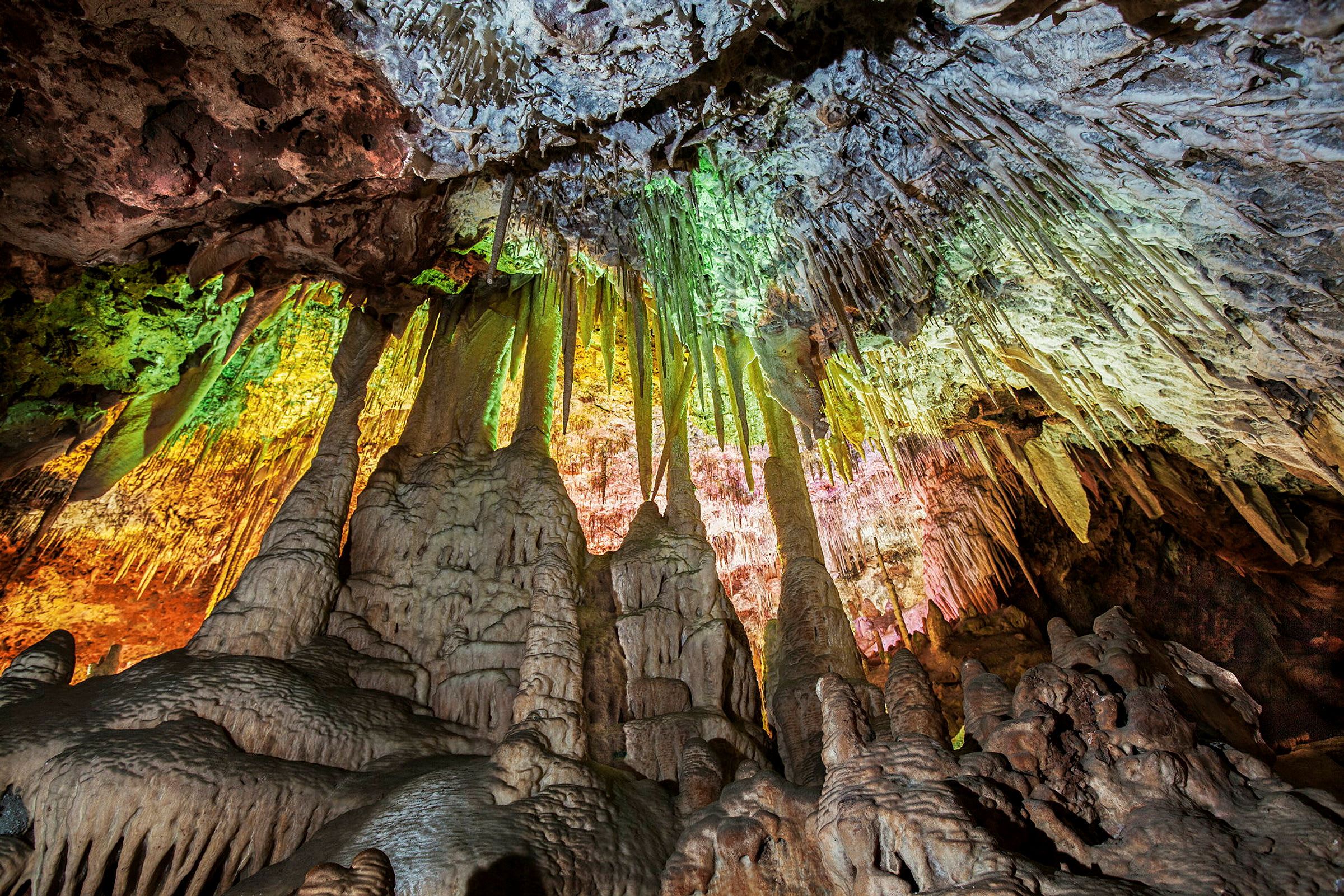 En grotta med stalaktiter och stalagmiter, belyst med färgade ljus. (AI-genererad text)