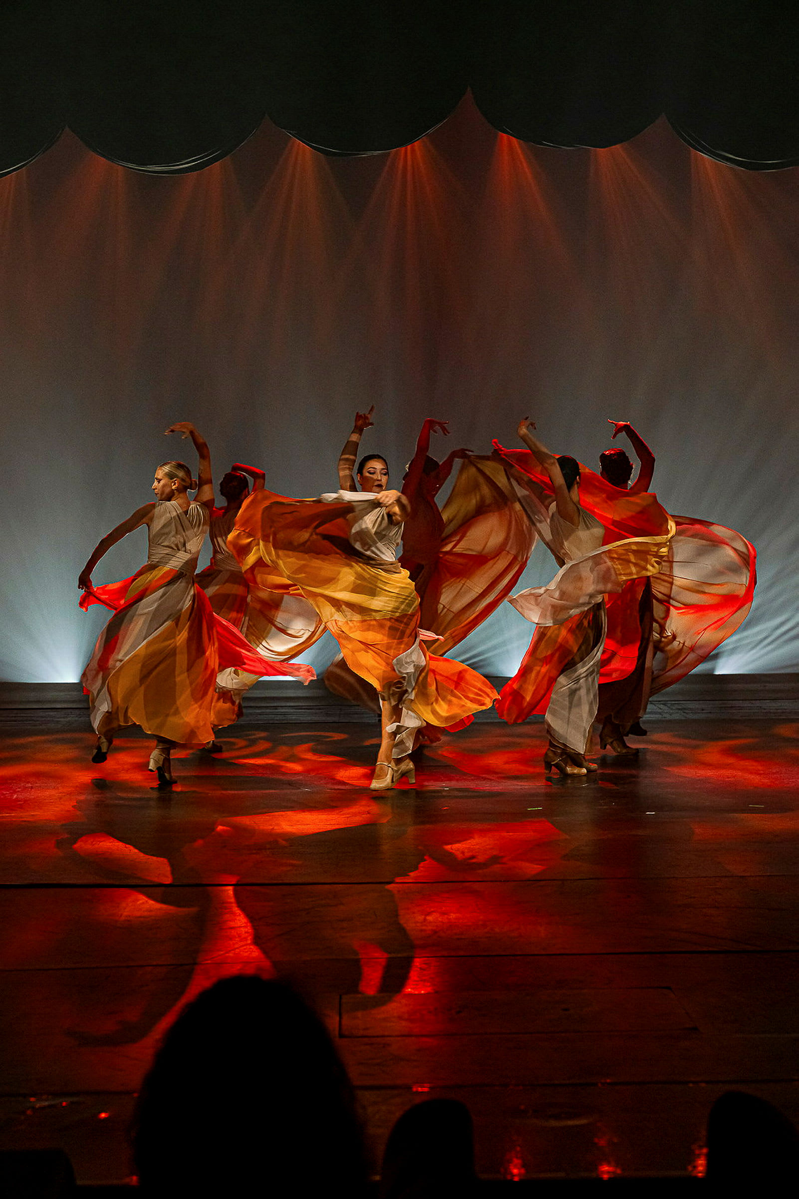En grupp dansare framför en koreografi på en scen med röda och orange ljus. (AI-genererad text)