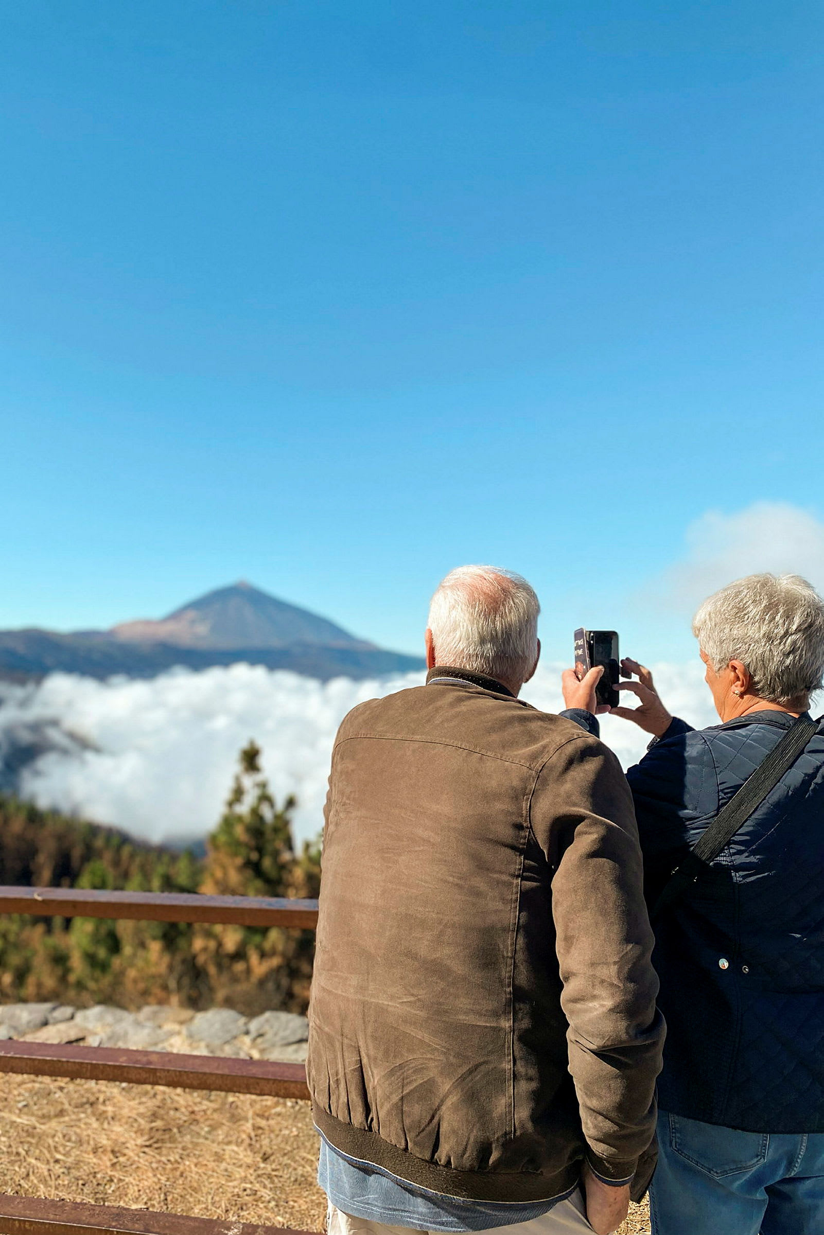 Två personer fotograferar utsikten med berg och moln. (AI-genererad text)