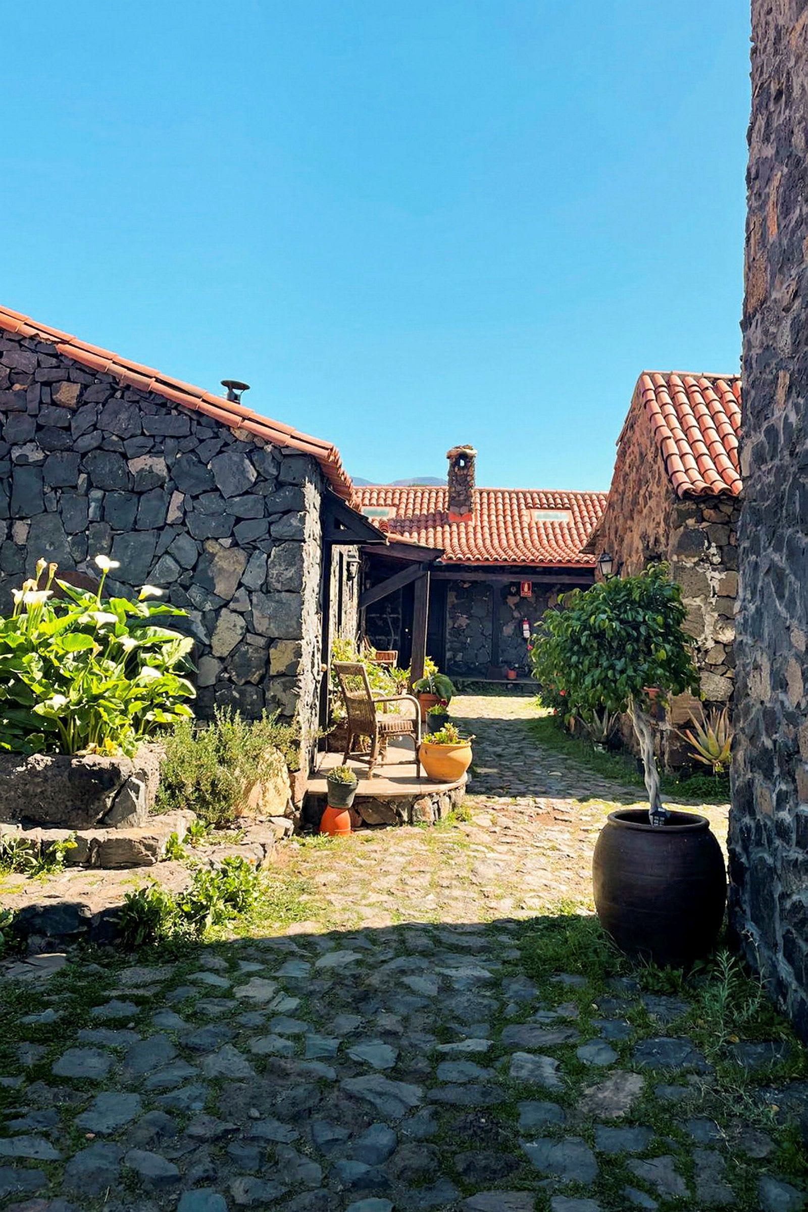 Gård med stenbelagda hus och terrakottatak, omgiven av växter och möblemang. (AI-genererad text)