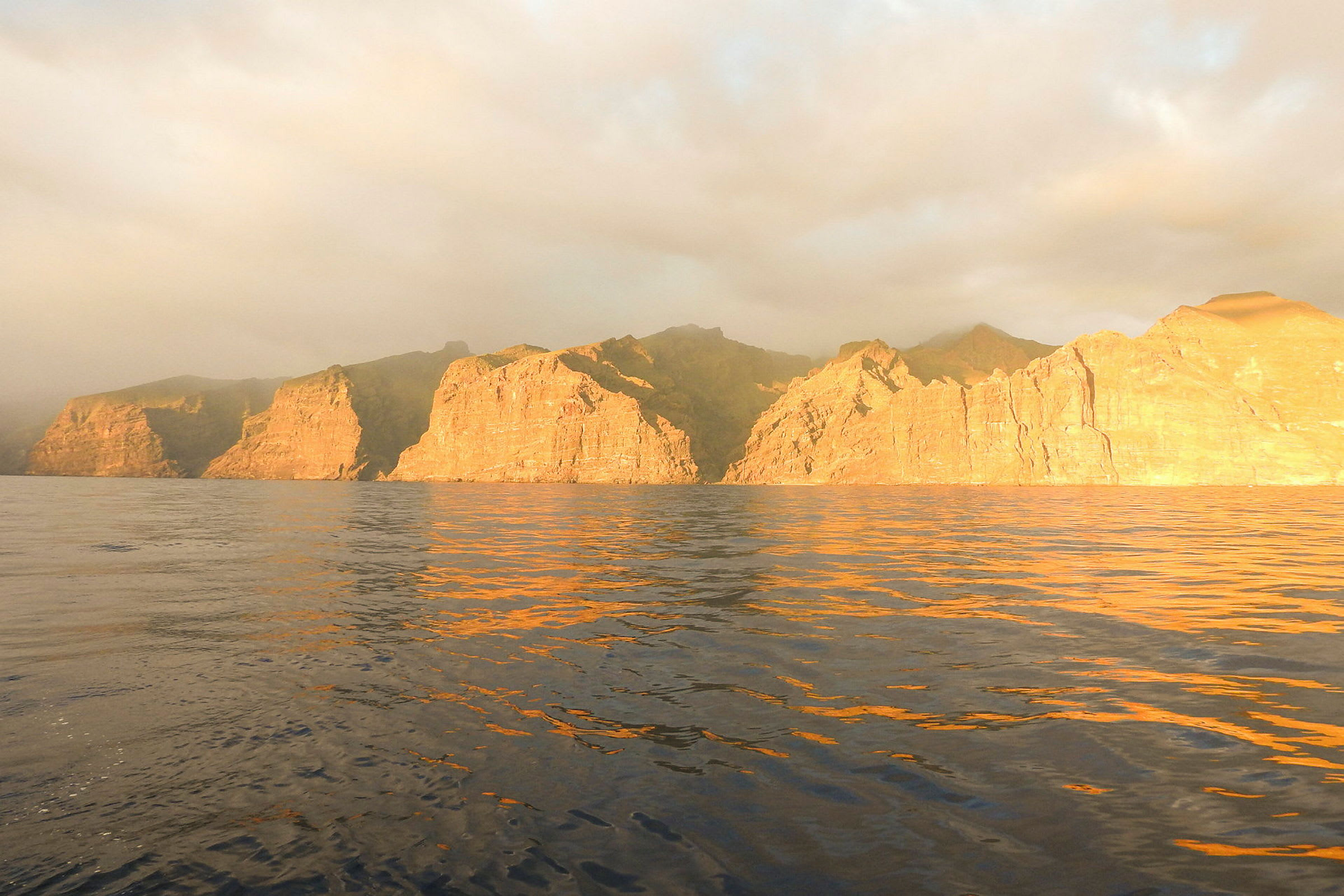 Solbelysta klippor vid havet under molnig himmel. (AI-genererad text)