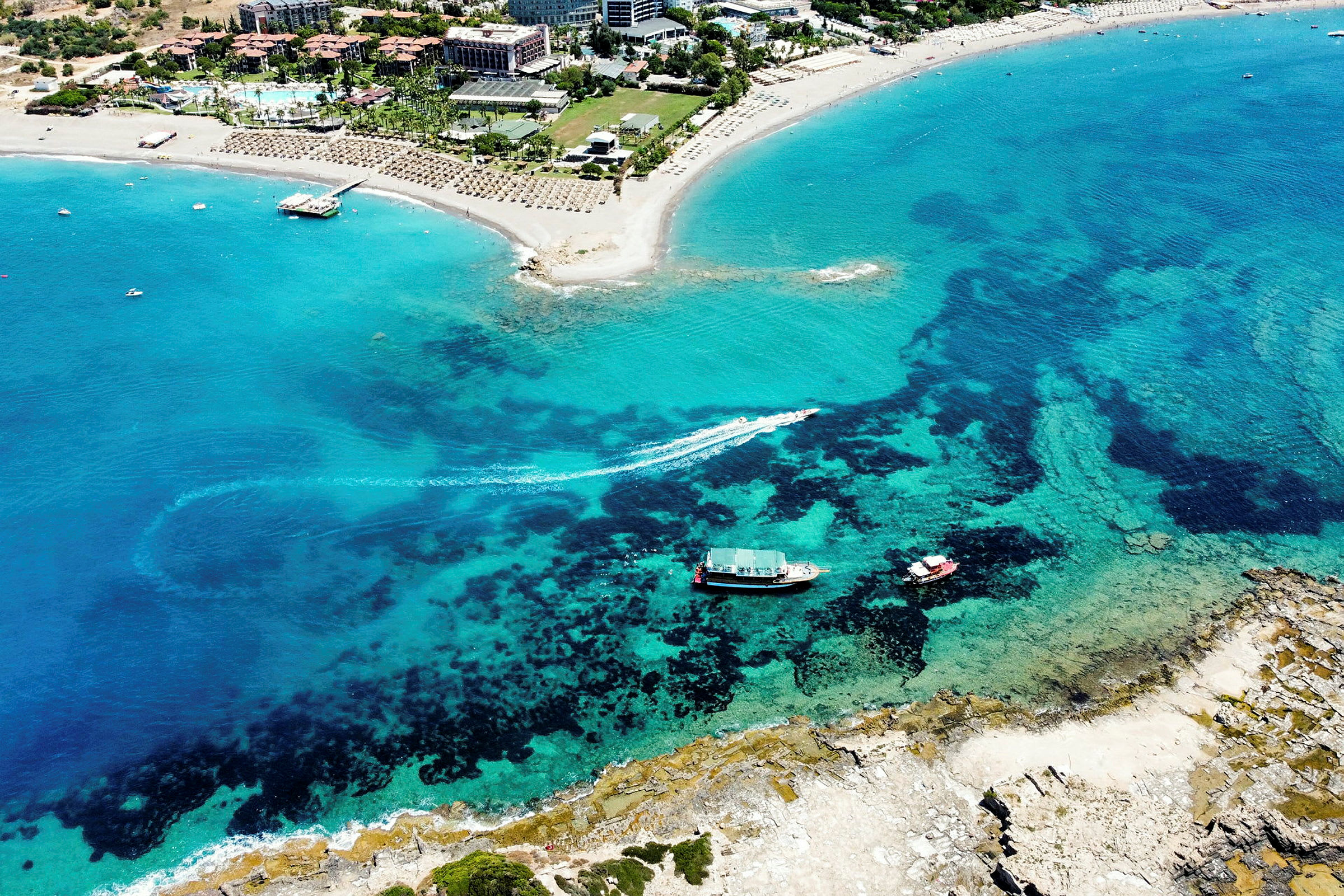 Flygfoto av en sandstrand vid ett turistområde, med klart blått vatten. (AI-genererad text)