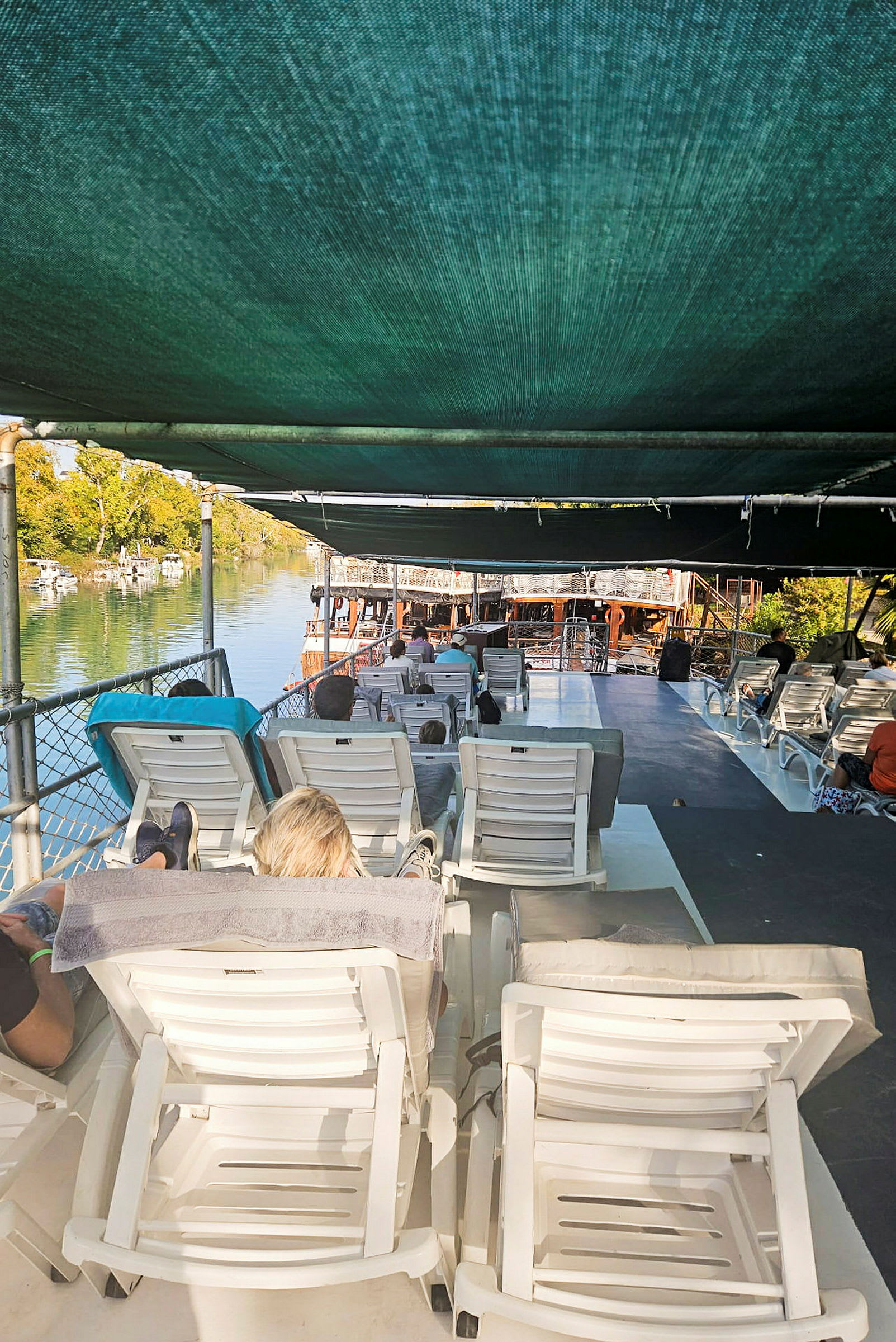 Personer som ligger på solstolar under ett skuggande tak på en båt vid vattnet. (AI-genererad text)
