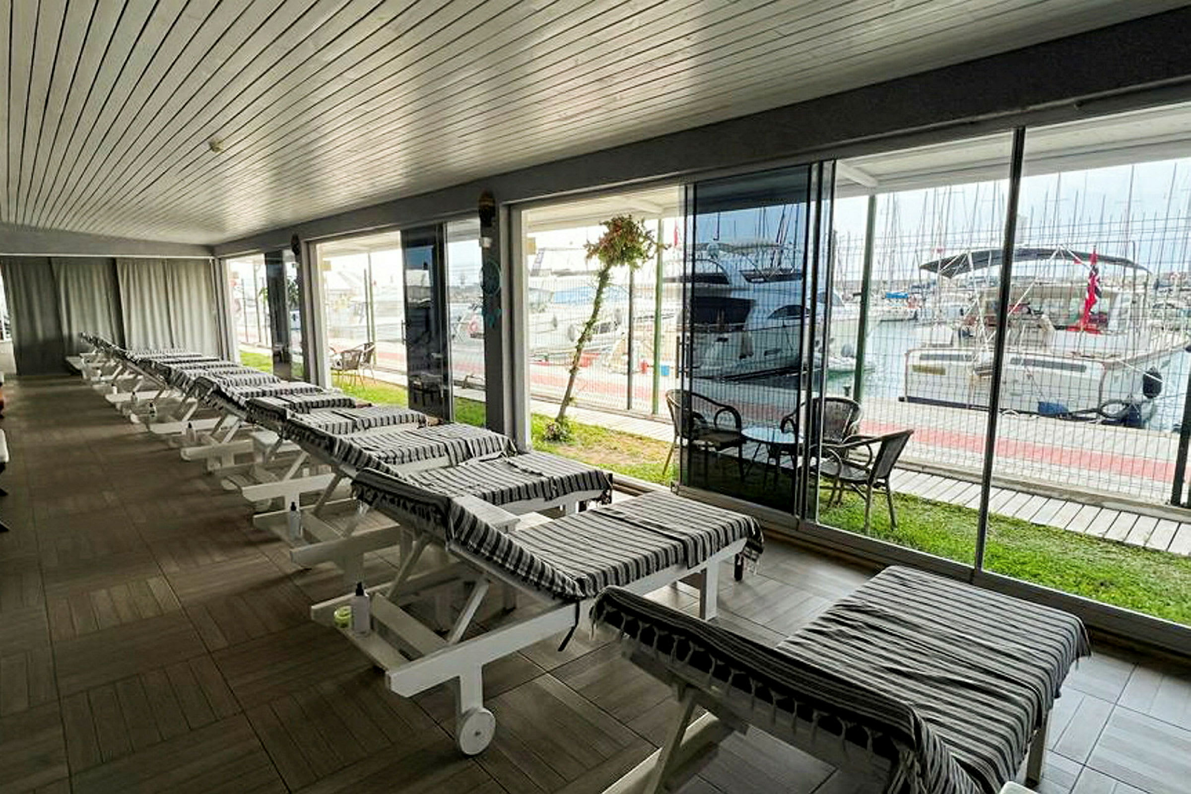 En ljus inomhusmiljö med vilstolar arrangerade i rader, utanför syns en marina med båtar. (AI-genererad text)