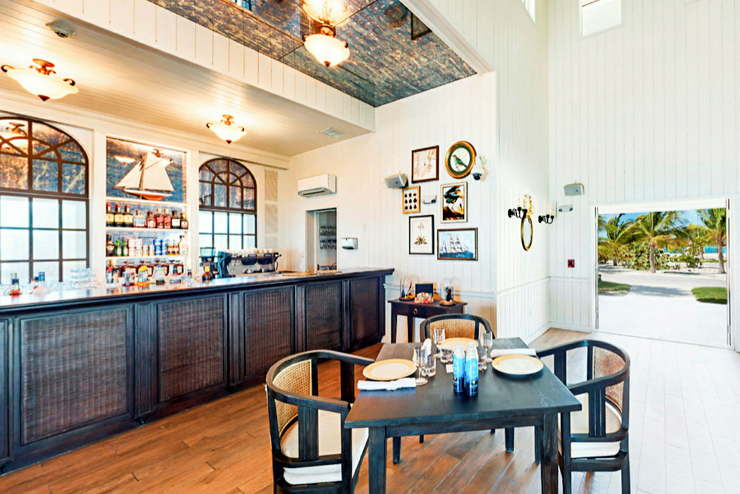 Ett inomhusområde med en bar, matbord, dekorationer på väggen och en öppning som visar utomhusmiljön. (AI-genererad text)